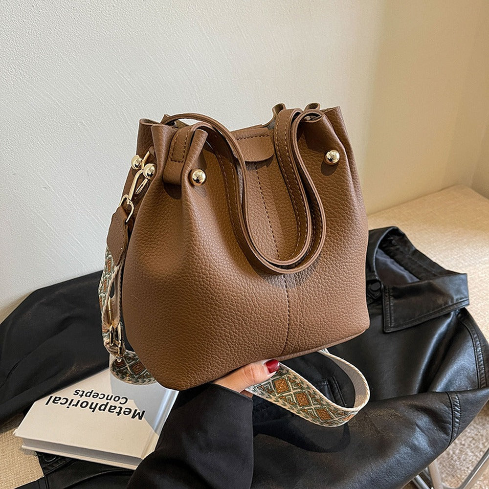 Brown bucket bag with top handles and wide crossbody strap